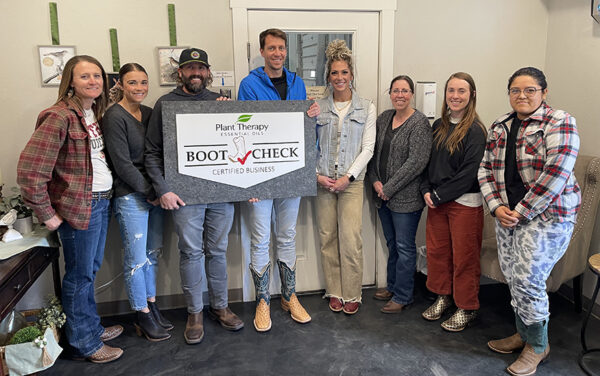 Chris Jones, third from left, and the staff of Plant Therapy pose with a sign showing the business is Boot Check certified, wherein employees of a business are encouraged to check on each other, promoting mental health. (PHOTO: PLANT THERAPY)