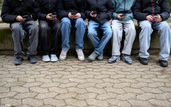 Teenagers pose for a picture while looking at their phones. Feb. 20, 2026. (PHOTO: REUTERS/Jana Rodenbusch)