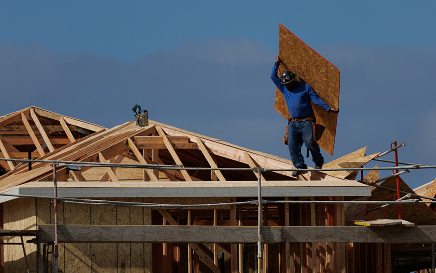 A construction worker carries a sheet of OSB sheathing as he builds a roof on a residential homes in Irvine, California, on March 28, 2025. (PHOTO: REUTERS/Mike Blake/File Photo)
